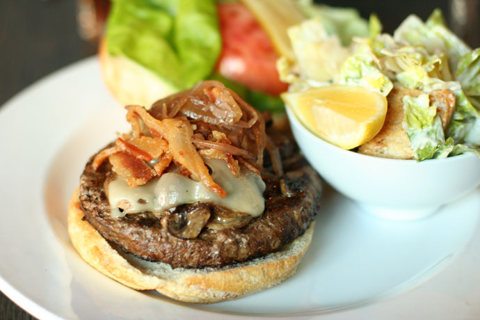 Hamburger with bacon, lettuce, onion, swiss cheese and a side Caesar salad.